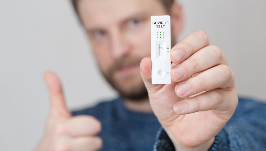 Hombre jóven con el pulgar hacia arriba muestra un test de covid negativo